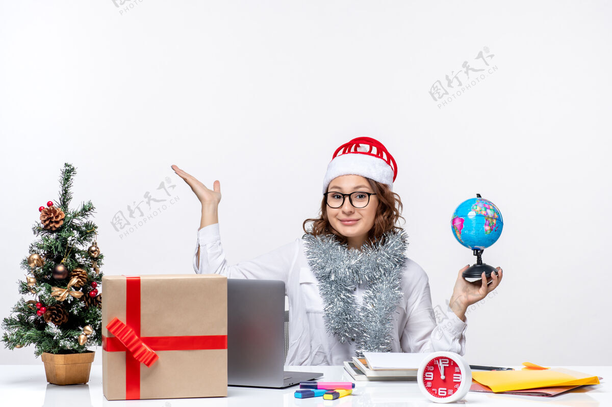 前面正面图：年轻的女工坐在她的位子前 手里拿着白色桌子上的地球仪抱着圣诞节商务