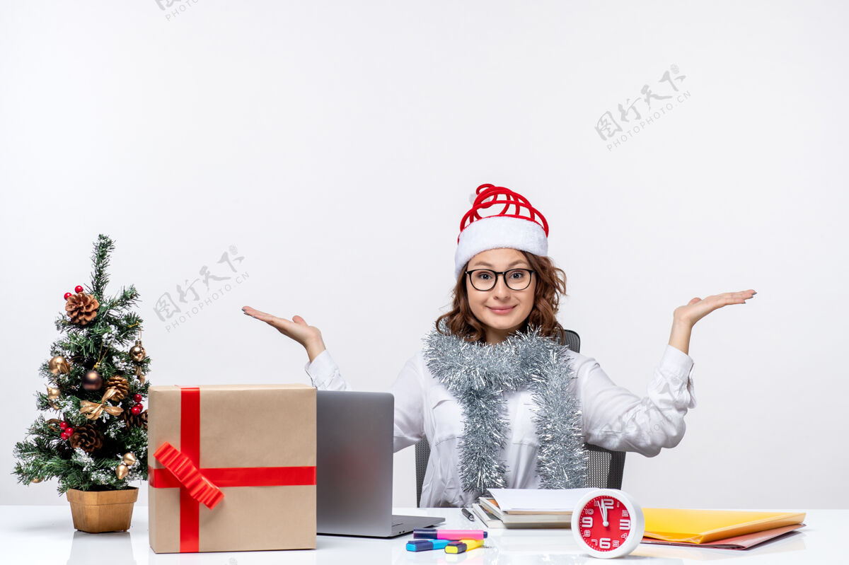 前面正面图：年轻女工坐在白色背景下的工作场所前帽子圣诞节桌子