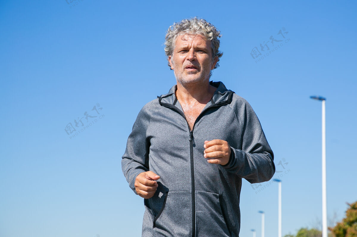 完整疲惫的白发男人穿着运动夹克在外面慢跑高级慢跑训练在早晨正面视图 蓝天 复制空间活动和年龄概念成熟出汗夹克