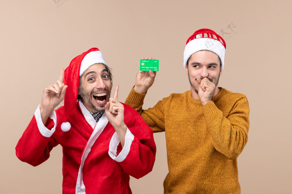 微笑前视图两个快乐的家伙一个穿着圣诞老人外套 另一个用信用卡闭上嘴 背景是米色的米色肖像结束