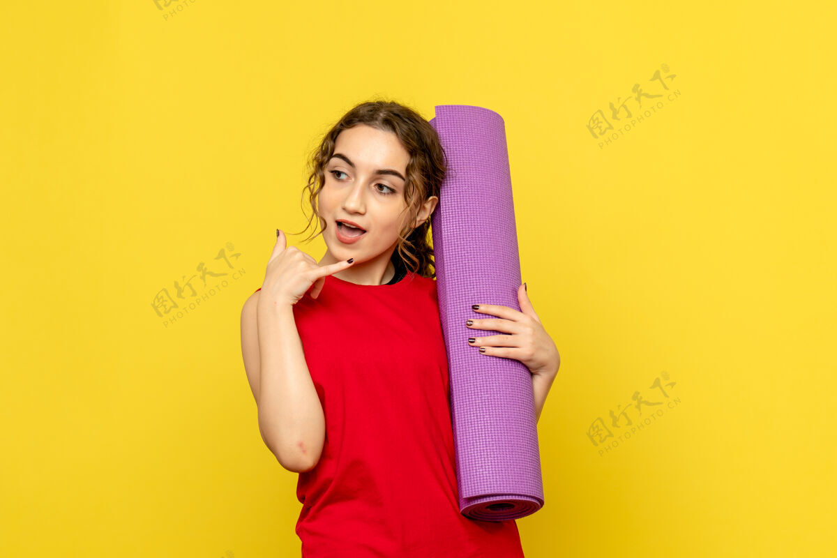 女人黄色墙壁上拿着紫色地毯的年轻女子的正视图情感肖像前面