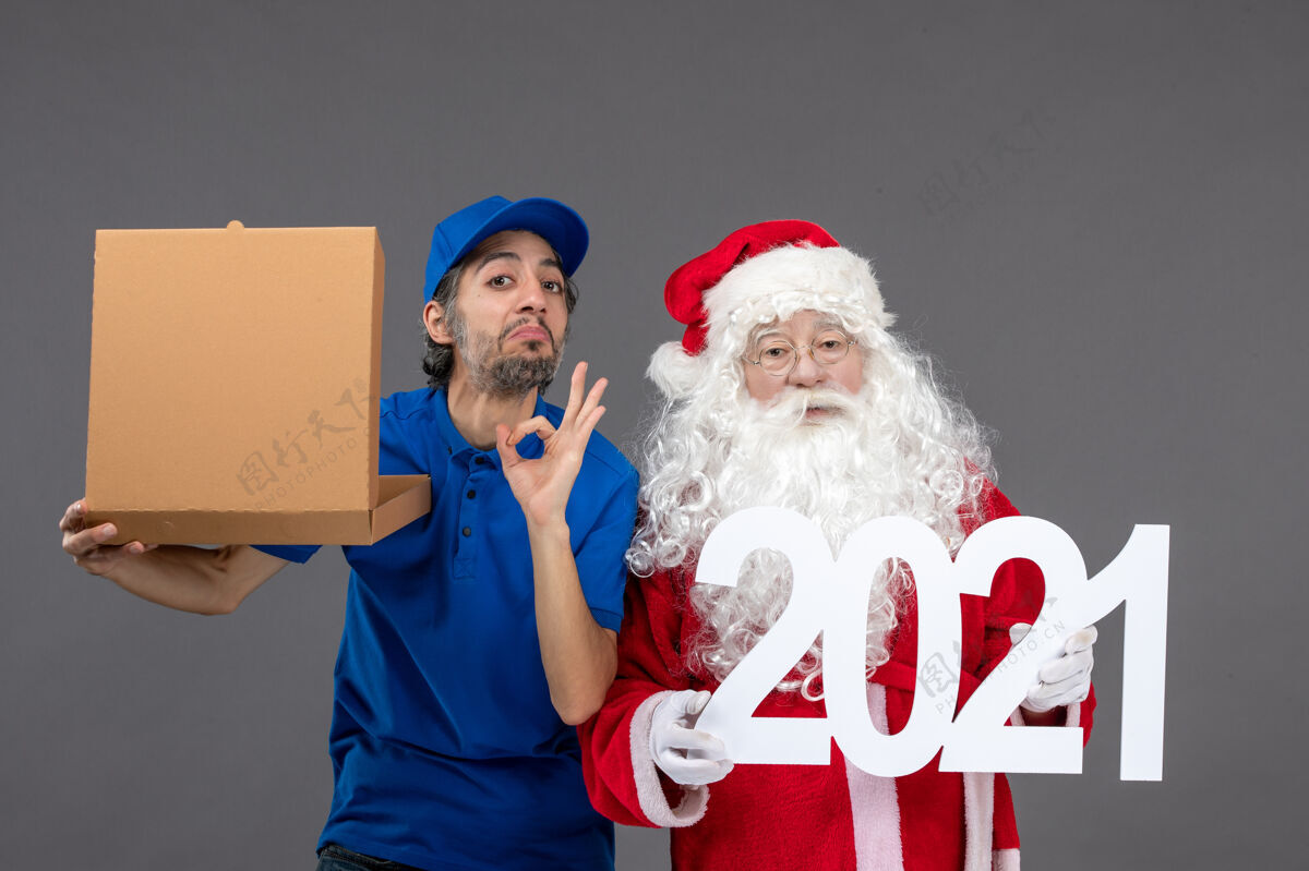 节日圣诞老人的正面图 男信使拿着食物盒 站在灰色的墙上快乐庆祝快乐