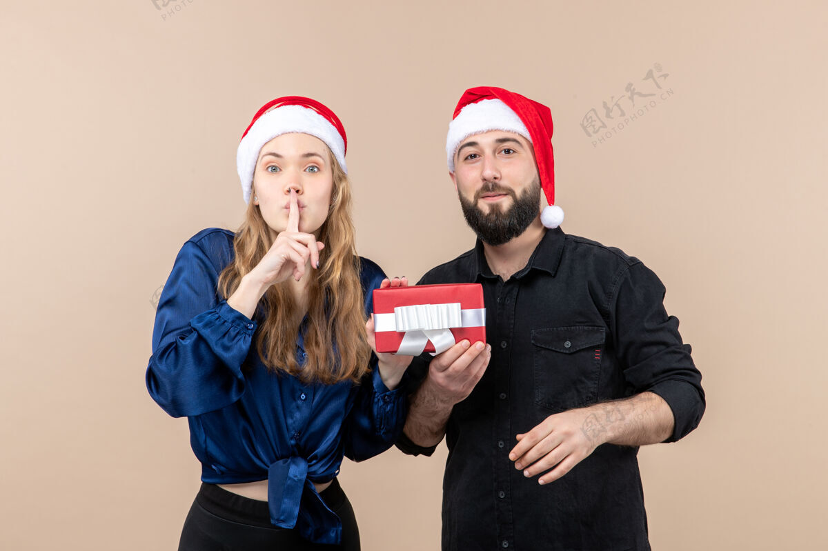 圣诞节年轻女子的正面图 粉红色的墙上有两个男人拿着礼物给她帽子圣诞快乐男