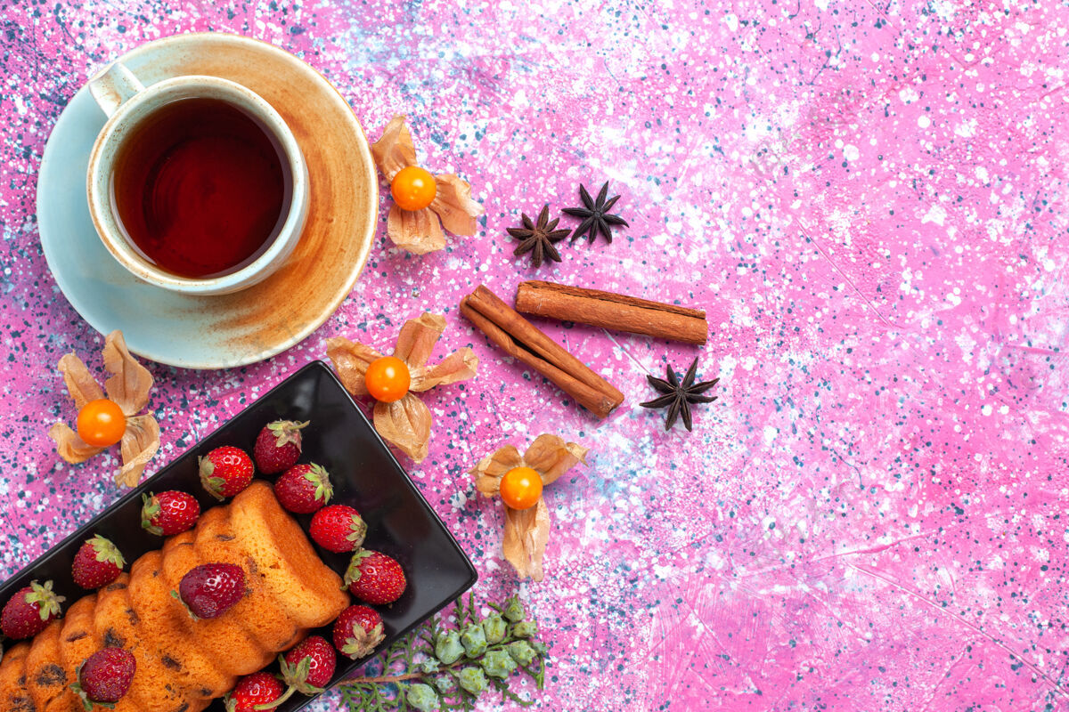 水果俯瞰美味的蛋糕在黑色蛋糕锅里 新鲜的红色草莓肉桂和茶放在粉红色的桌子上甜味茶肉桂