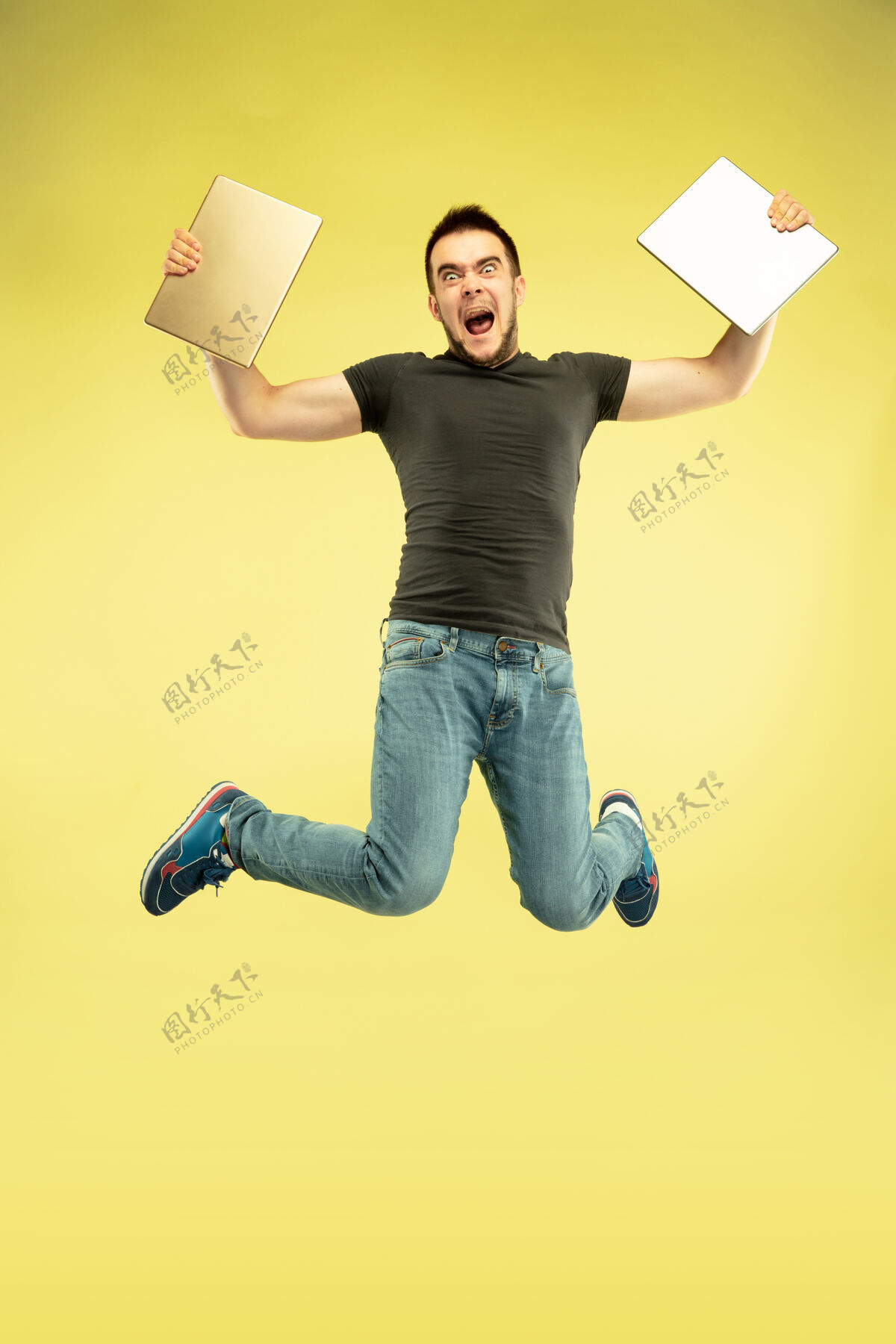跳跃失重全长的快乐跳跃的人与黄色背景上孤立的小玩意画像现代科技 自由选择的概念 情感的概念使用自拍或飞行中的vlog平板电脑设备平板电脑连接