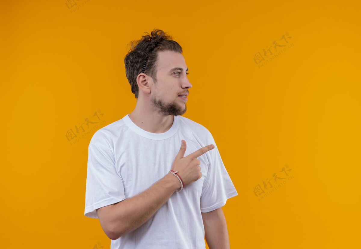 男看起来年轻人穿着白色t恤指向一边孤立的橙色背景T恤白色侧