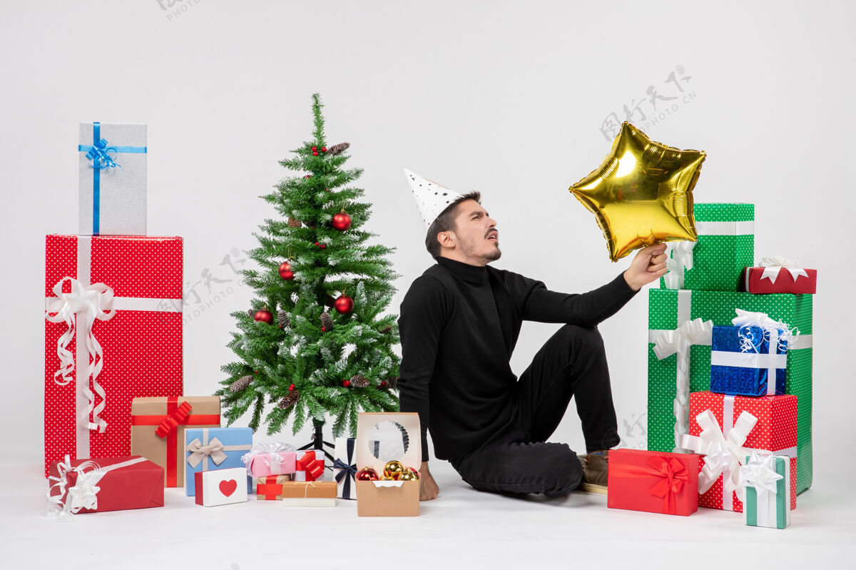 圣诞节年轻人围坐在礼物旁边 拿着金星在白墙上十二月礼物节日