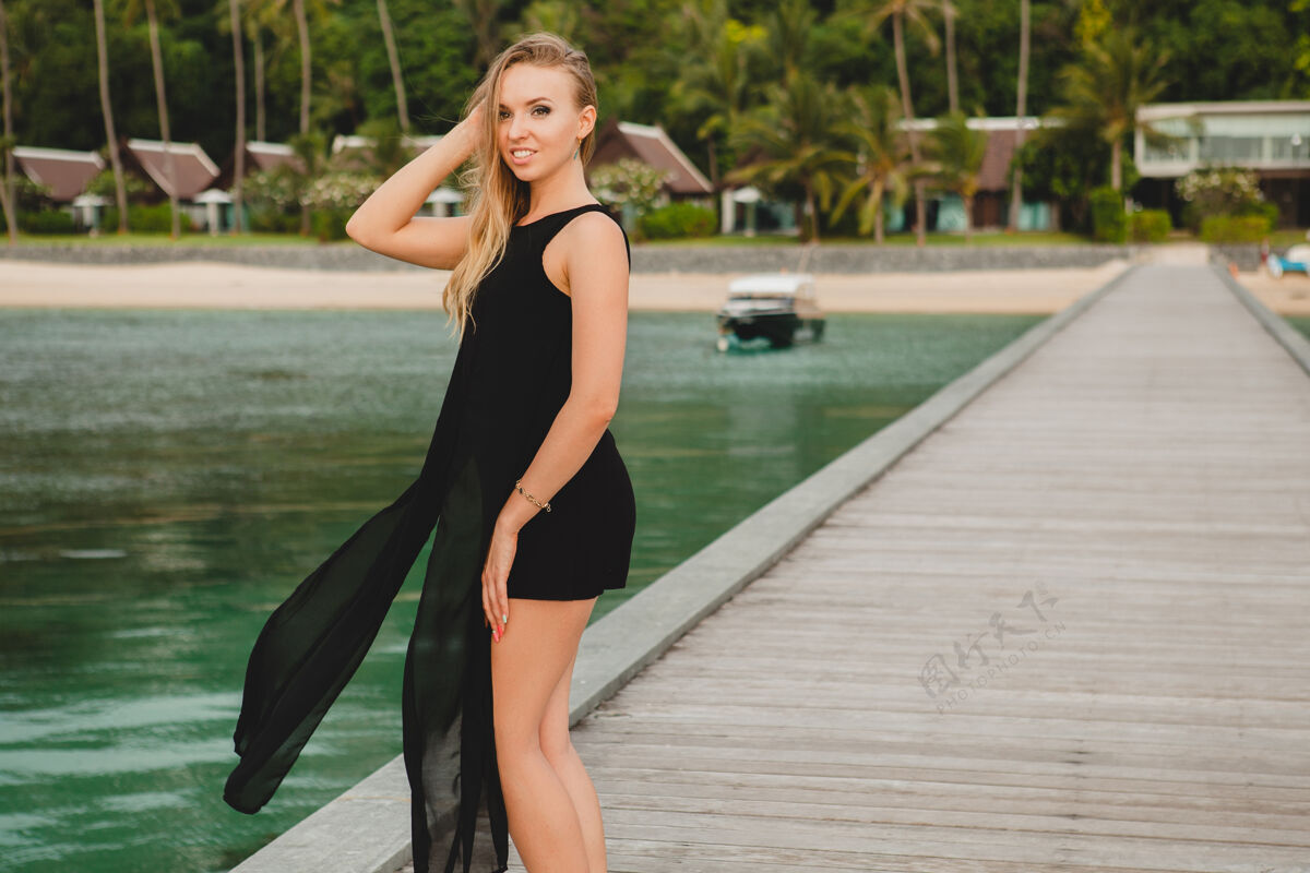 无忧无虑穿着黑色连衣裙的美丽迷人的女人在豪华度假酒店的码头上摆姿势 暑假 热带海滩海滩夏天岛屿