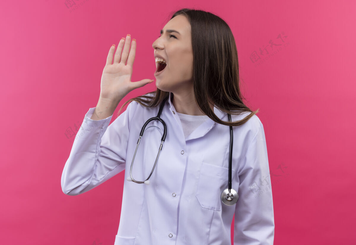 女孩看着身边穿着听诊器医用长袍的年轻医生女孩 在孤立的粉色背景下呼唤着某人粉红穿看