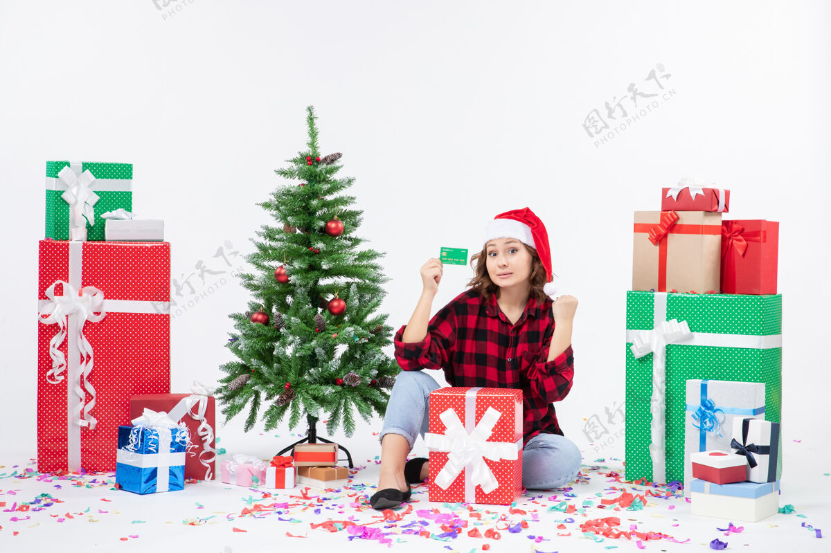 雪正面图：年轻女子围坐在白色墙上 手里拿着绿色的银行卡人圣诞节抱着
