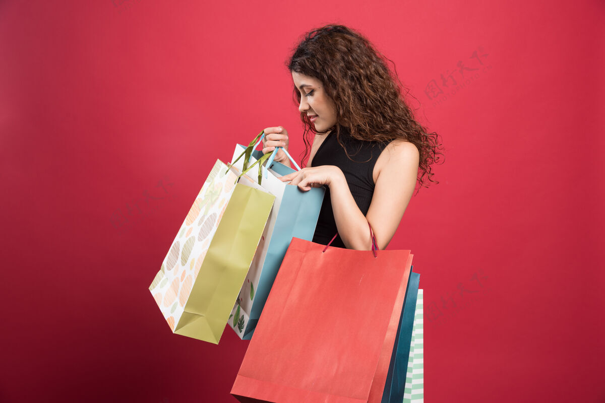 漂亮在红色背景上展示她的购物的女人高质量的照片女孩购物携带