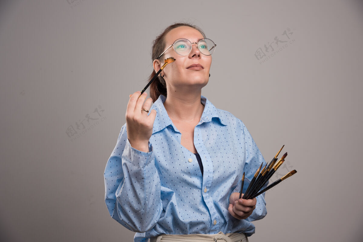 对象女画家拿着画笔在灰色背景上靠近她的脸画画设备