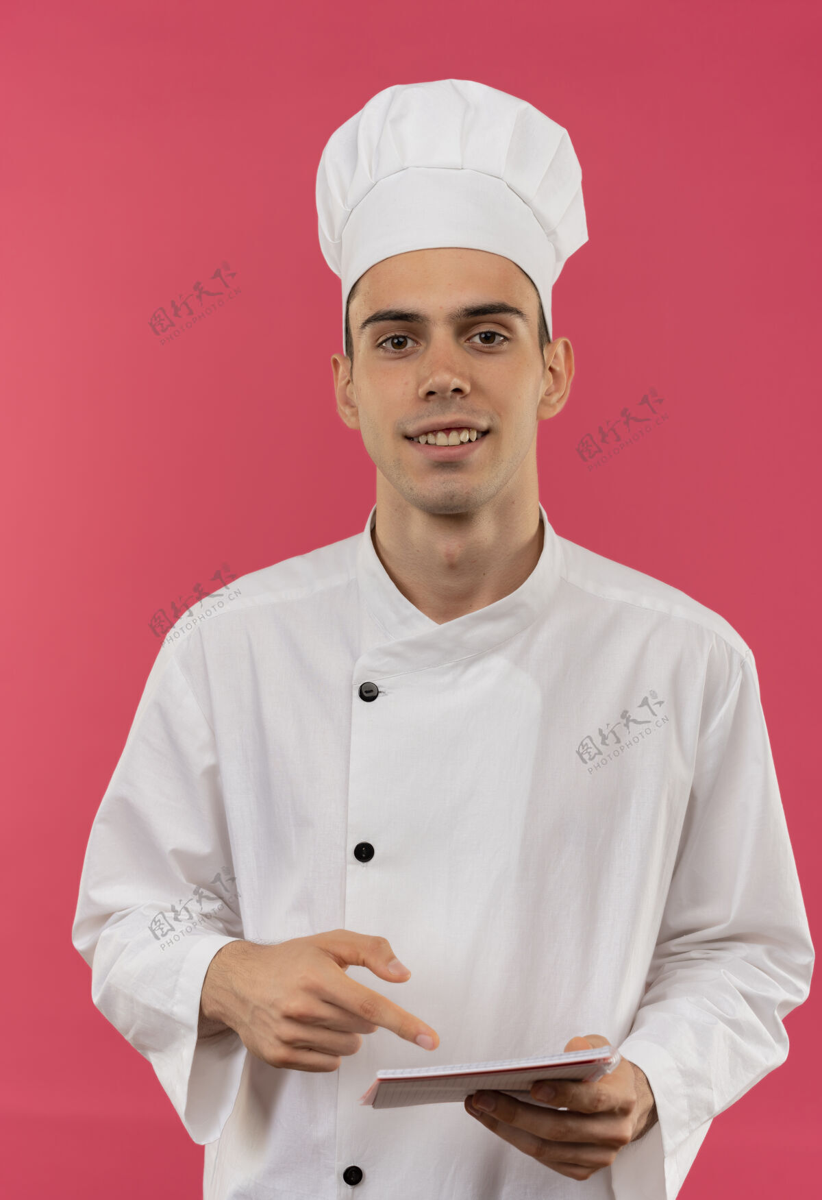 男面带微笑的年轻男厨师穿着厨师制服拿着并指着笔记本制服笔记本分