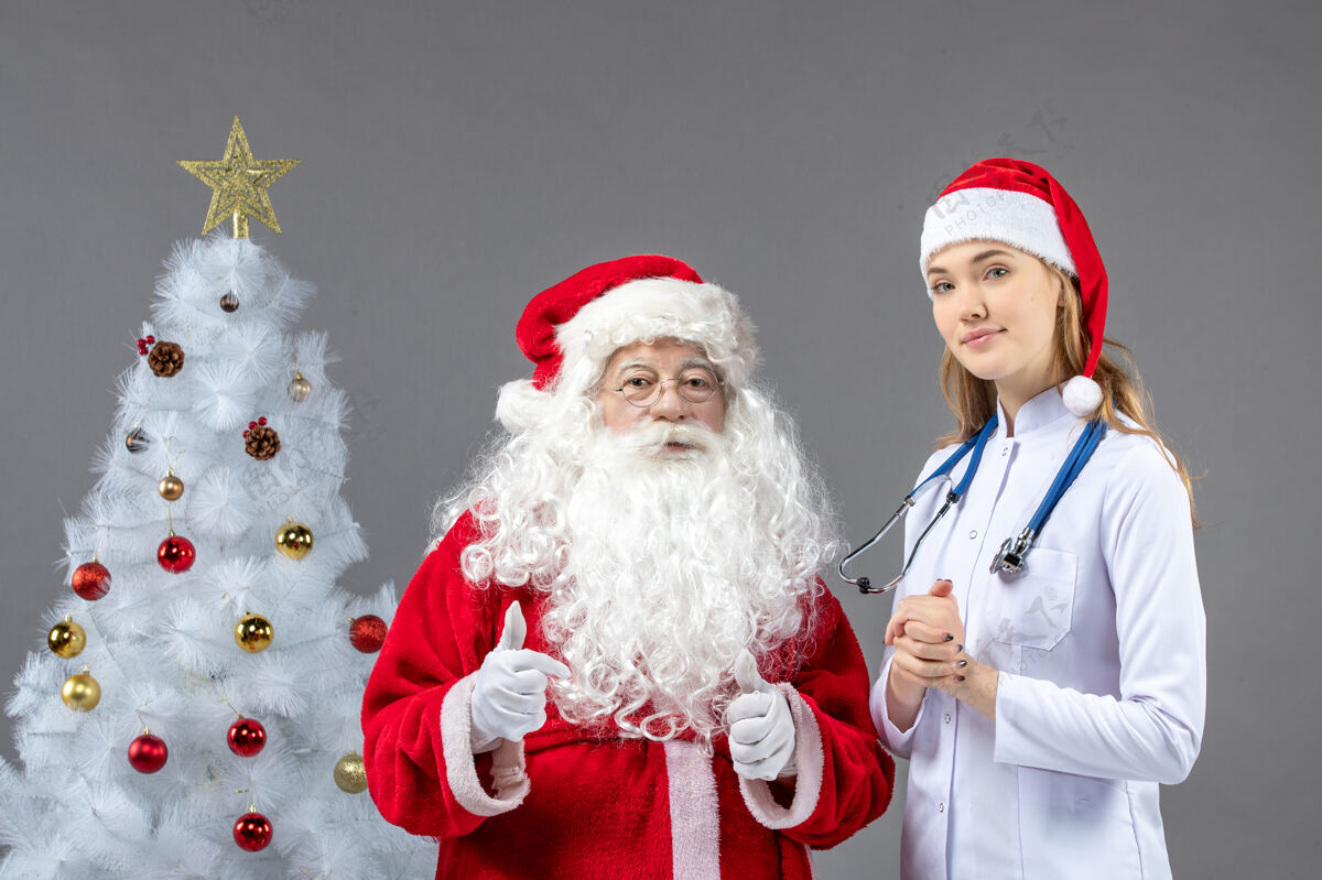 医疗圣诞老人和女医生的前视图 女医生正在灰墙上检查他的健康状况情况前面快乐