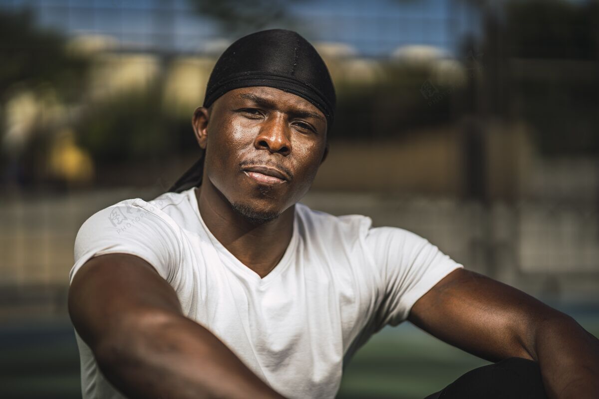 形状一个穿着白衬衫坐在篮球场上的非洲裔美国男子的特写镜头肌肉男性自信