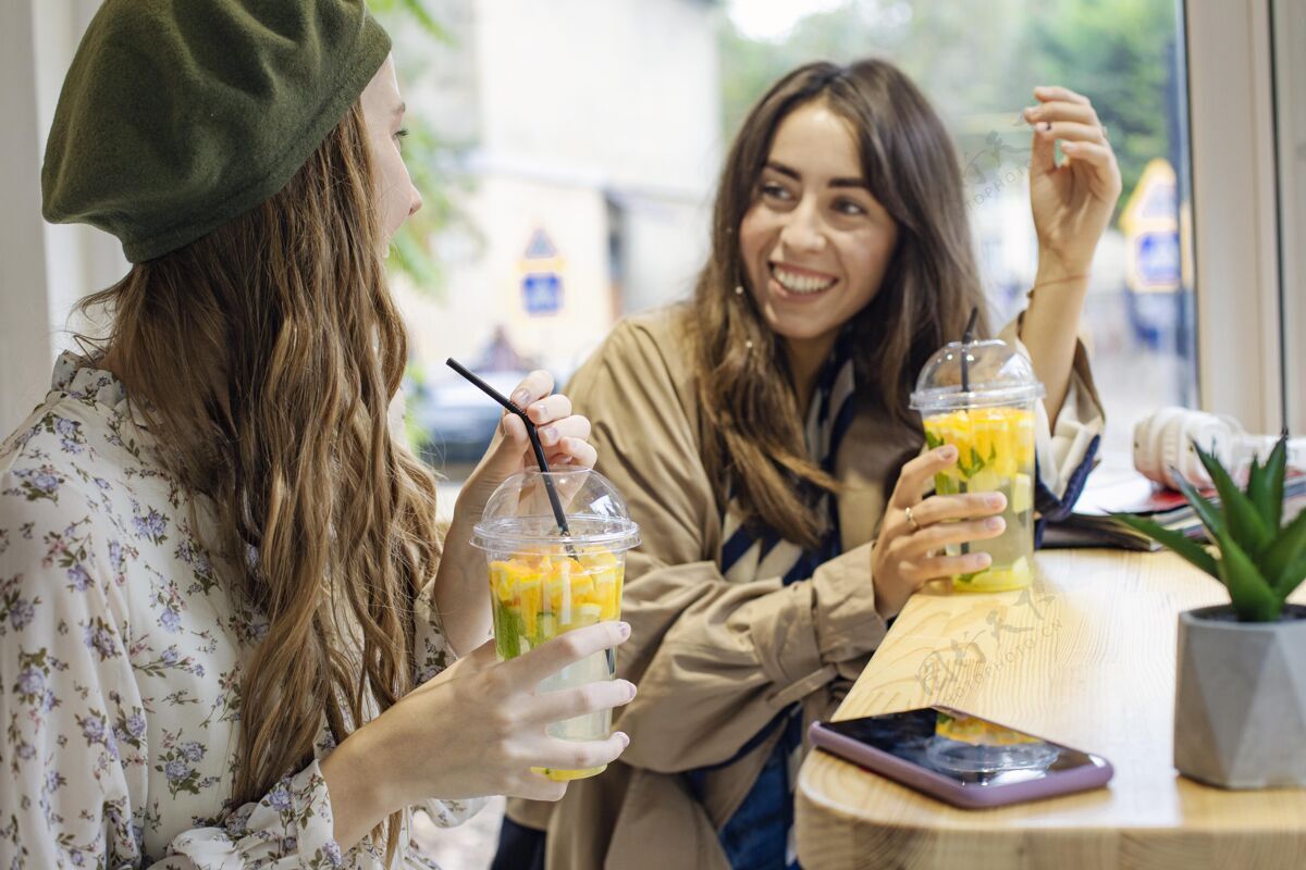 美味中镜头的女人们拿着新鲜的饮料在咖啡馆聊天美味热带健康