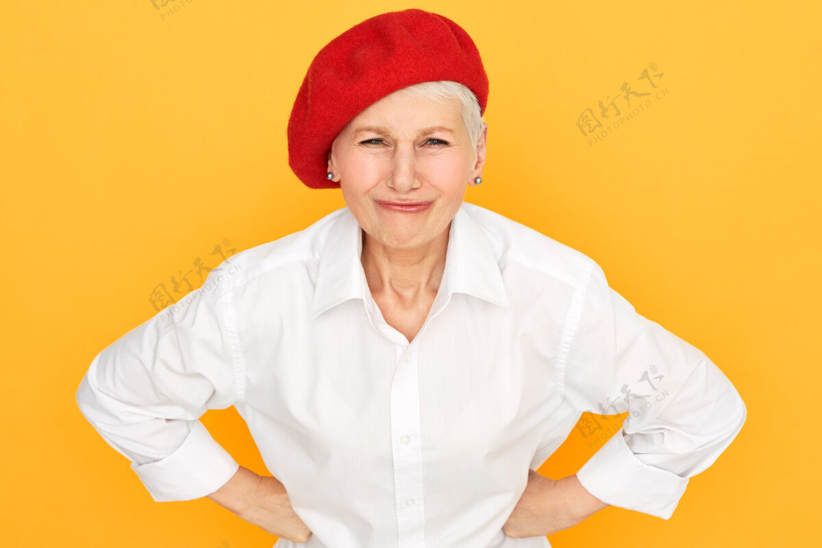 女性不满的短发女性退休者的肖像 戴着优雅的红色帽子 手放在腰上年老表情问题