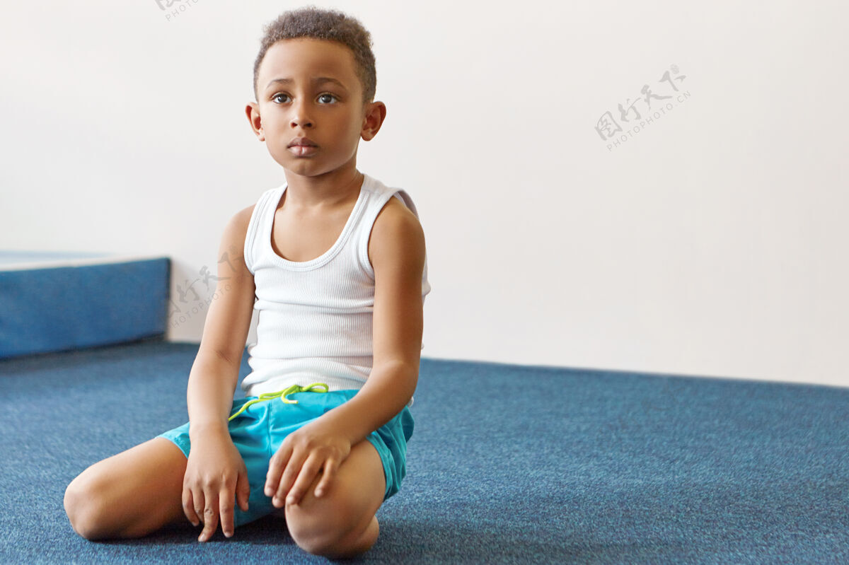 健康一个可爱的非洲裔美国男孩穿着T恤和短裤坐在他的脚后跟孤立的镜头儿童姿势健身