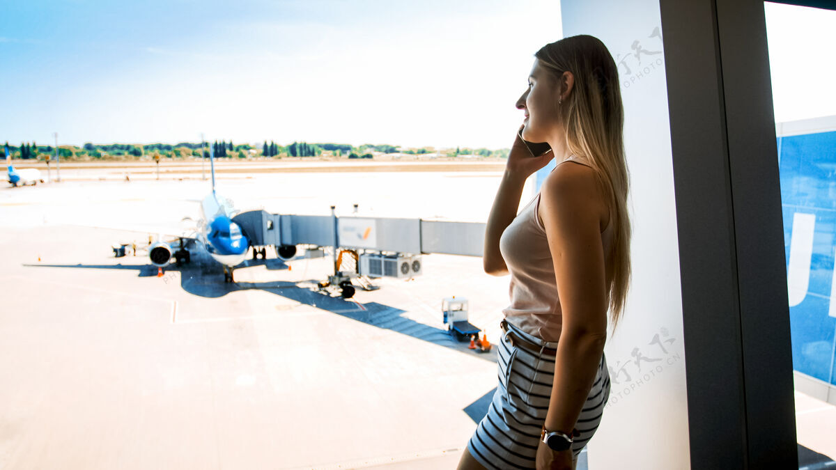 飞机站在机场候机楼窗口打电话的漂亮年轻女子女性专业人士终点站