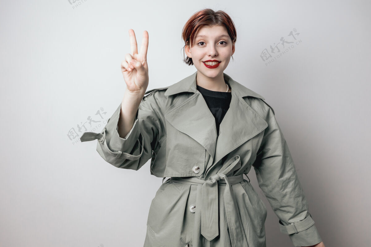 大一个穿着时髦绿色外套的开朗女孩展示了胜利的标志女人学生微笑