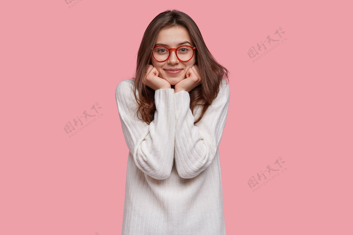正面快乐的女人双手托着下巴 戴着红边眼镜和白色长毛衣 脸上带着温柔的微笑漂亮外表毛衣