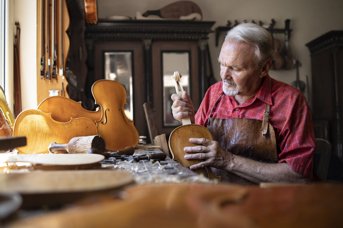 大师高级木匠在他的木匠车间组装小提琴乐器的零件锯末木制品制作