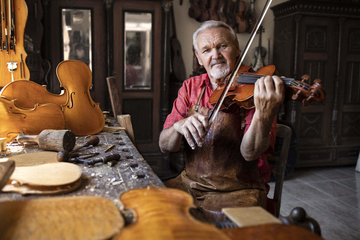 高级工匠检查质量和拉小提琴在他的旧时尚木匠工作室小提琴手工工具