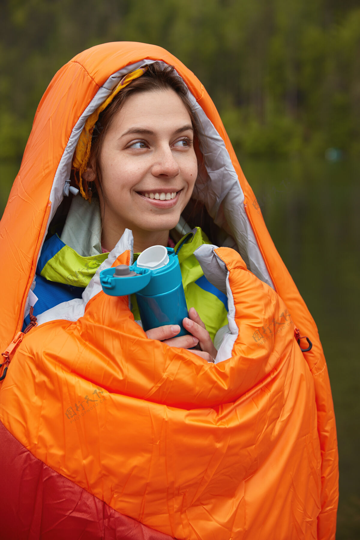 山地人们和露营的概念高兴可爱的女徒步旅行者包裹在橙色睡袋 温暖自己在寒冷的日子徒步旅行女性活动