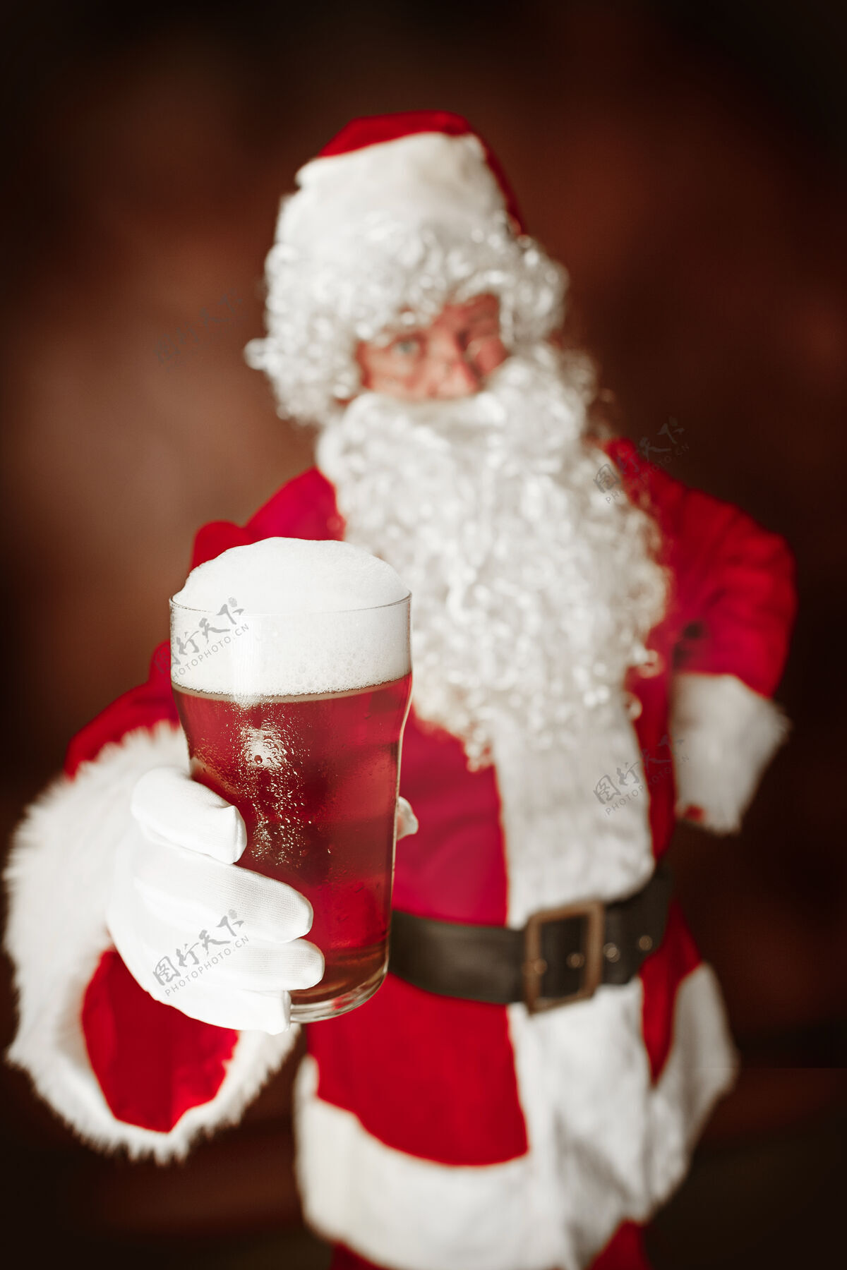 圣诞老人穿着圣诞老人服装的人的肖像-一个豪华的白胡子 圣诞老人的帽子和红色服装在红色工作室背景与啤酒老年人圣诞节圣诞老人