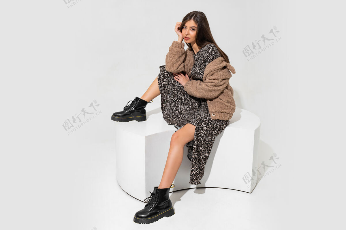 好看优雅的欧洲女人穿着冬天的皮草外套和时髦的裙子坐着穿着黑色皮革的踝靴服装模特冬天