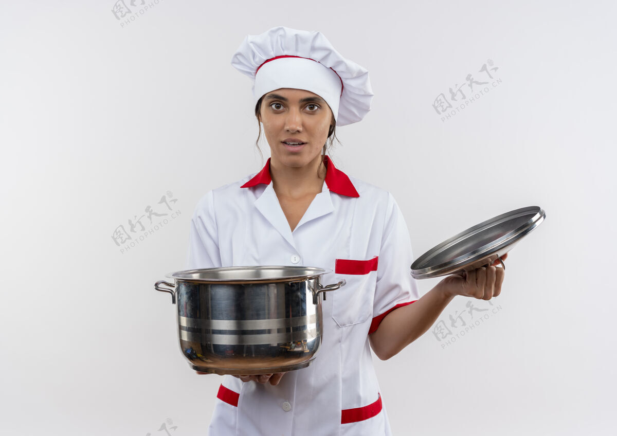 年轻年轻的女厨师穿着厨师制服拿着平底锅和盖子在隔离的白色墙壁上复制空间厨师厨师看着
