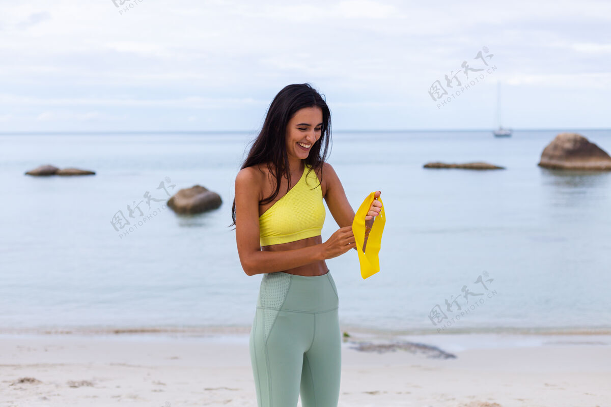 迷人海滩上穿着五颜六色运动服的迷人年轻女子体重人健康