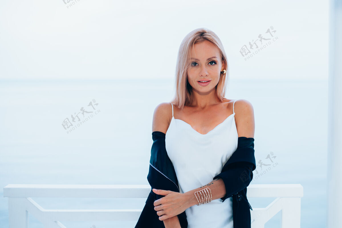 年轻时尚写真时尚的白种女人在丝绸长裙黑色外套豪华的地方与海景风格时尚外观