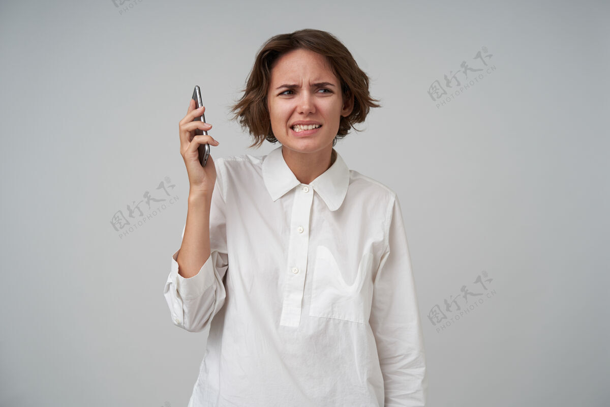 手机室内镜头：一位棕色短发的年轻女士在电话里说脏话 撅着嘴 扭着嘴 穿着正装站在一旁衣服撅嘴心情