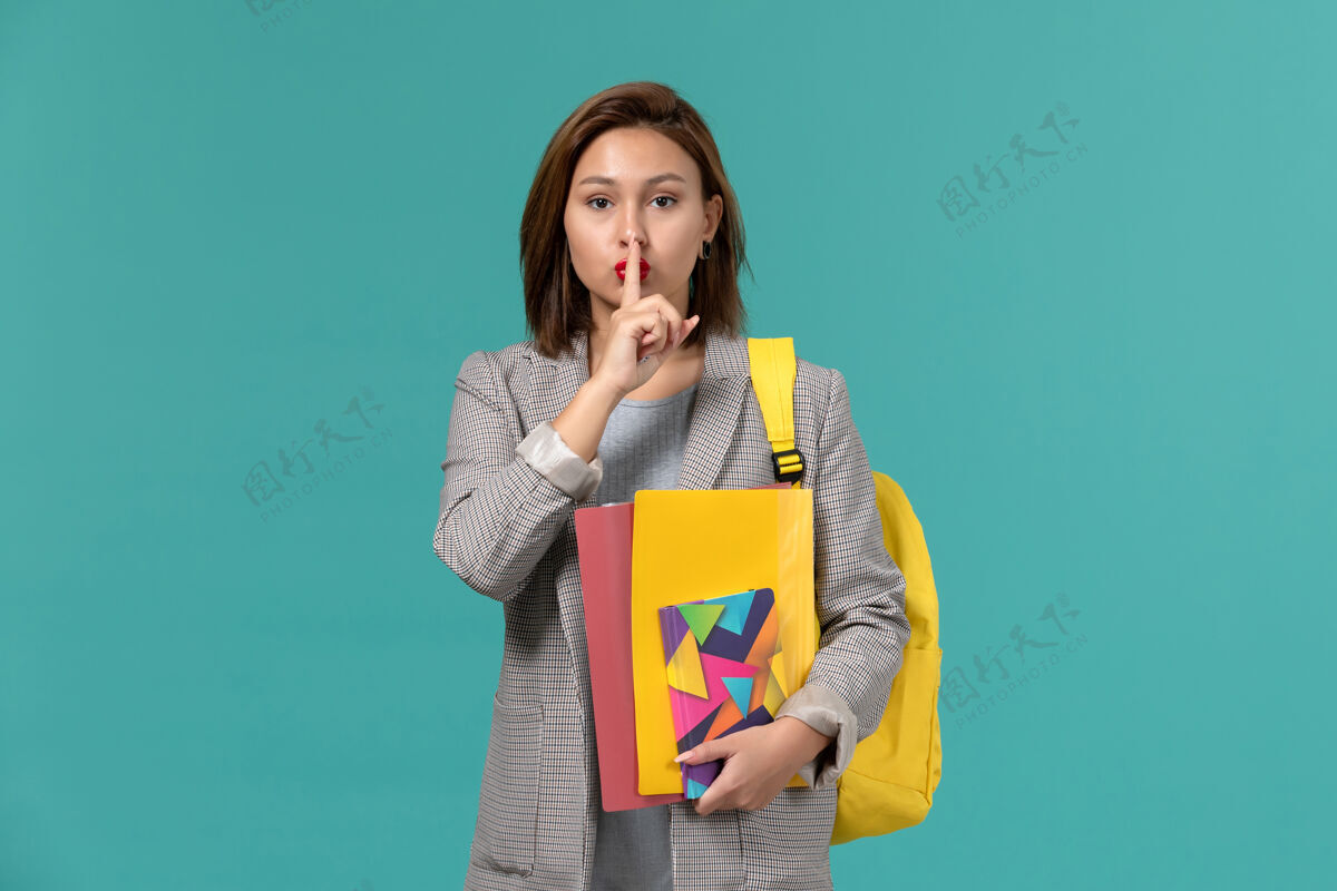 档案身着灰色夹克 背着黄色背包 在蓝色墙上拿着文件和文案的女学生的正视图学院学校正面