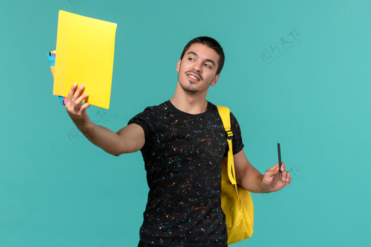 光身穿深色t恤黄色背包的男学生正面图 浅蓝色墙上有文件和抄写本人正面教训