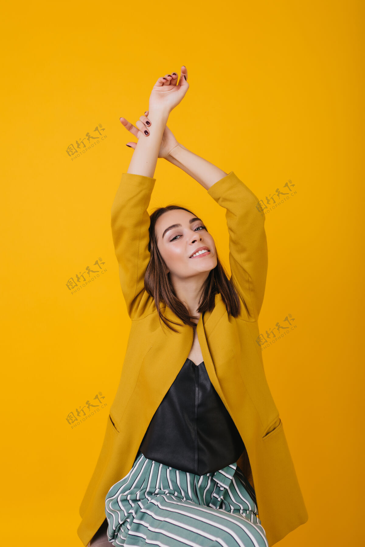 优雅快乐的白人女子穿着优雅的黄色夹克 举手合影嬉皮的黑发白人女孩的室内照片快乐快乐美丽