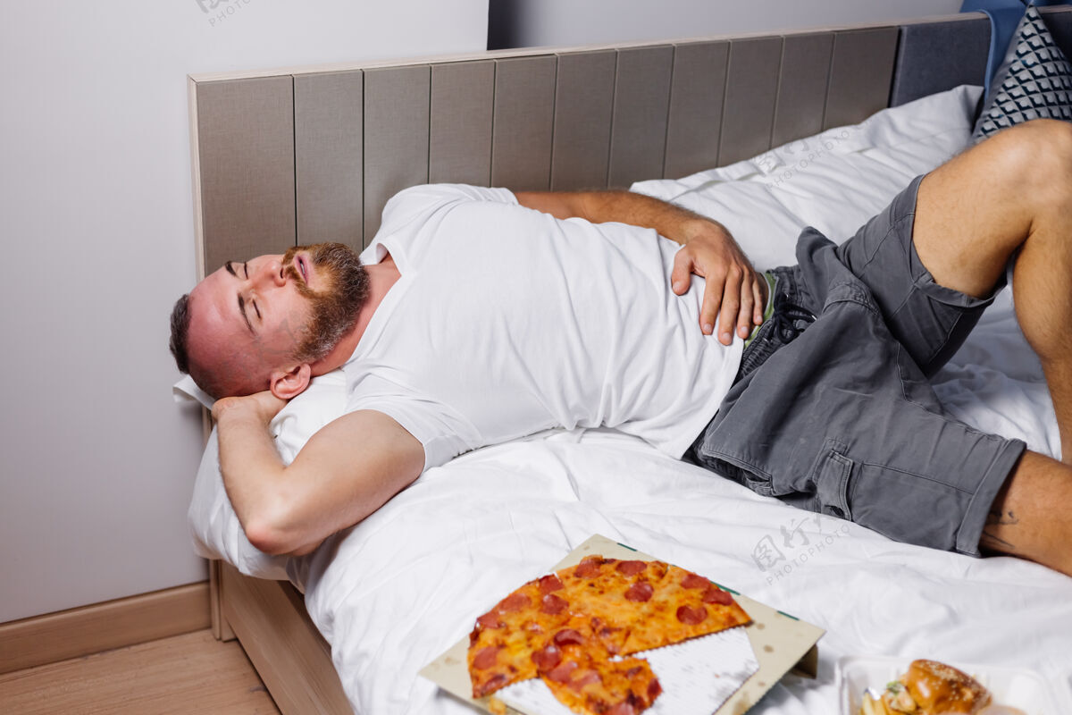 吃饭一个留着大胡子的白种人在吃过多的快餐比萨饼和汉堡后躺在床上披萨吃休闲
