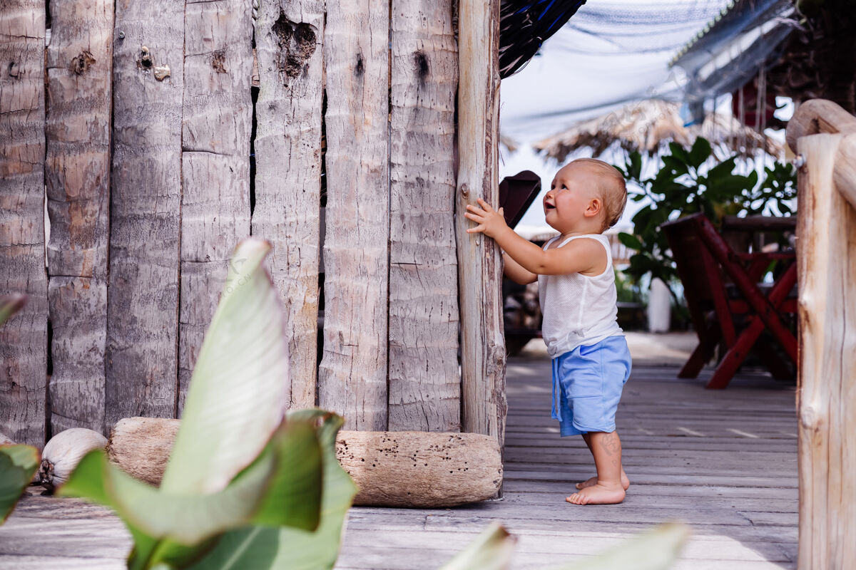 夏天穿着蓝色短裤和白色衬衫的九个月大的快乐孩子的户外肖像站在木墙上微笑着微笑快乐户外