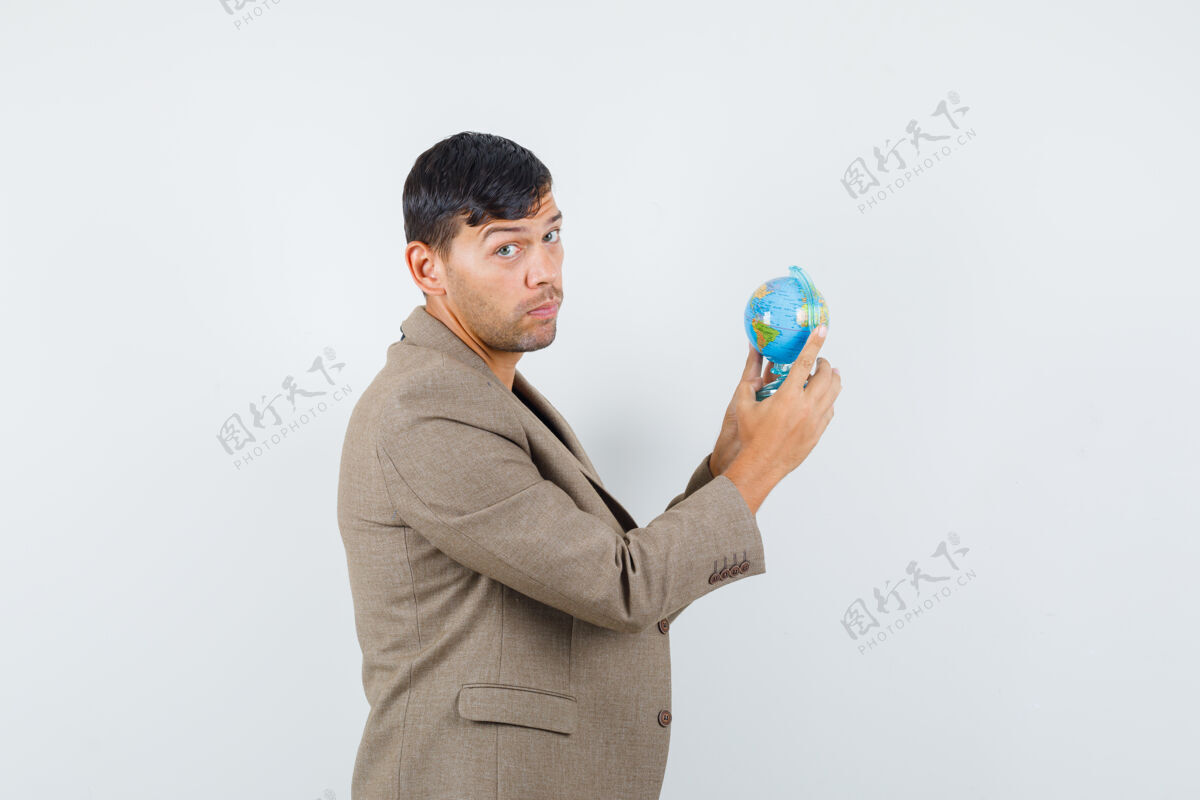 地球地球身穿灰褐色夹克 黑色衬衫的年轻男子一边看着一边 一边拿着迷你地球仪 神情迷茫 前视图抱着帅气地图