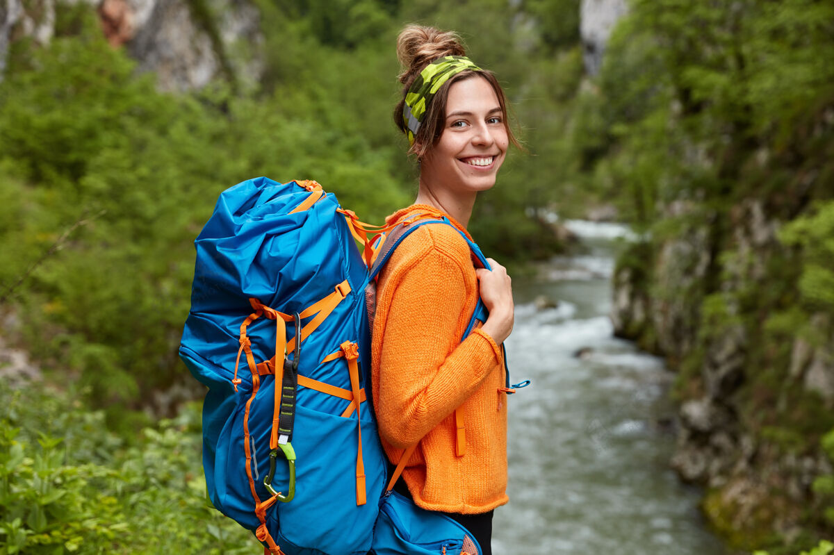 河流穿着橙色套头衫的快乐女人的侧身镜头 徘徊在山河附近人类山脉秋天