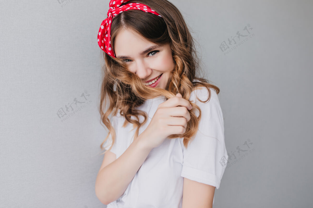 波浪发有兴趣的漂亮女孩摆出害羞的微笑室内照片的情感卷发女子戴着红丝带兴奋浪漫卷发