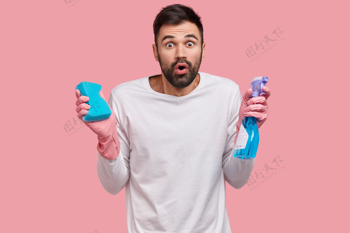 害怕表情惊恐的情绪化未刮胡子的男人 拿着一瓶洗涤剂和海绵 做家务 参与春季大扫除家务清洁剂情绪化