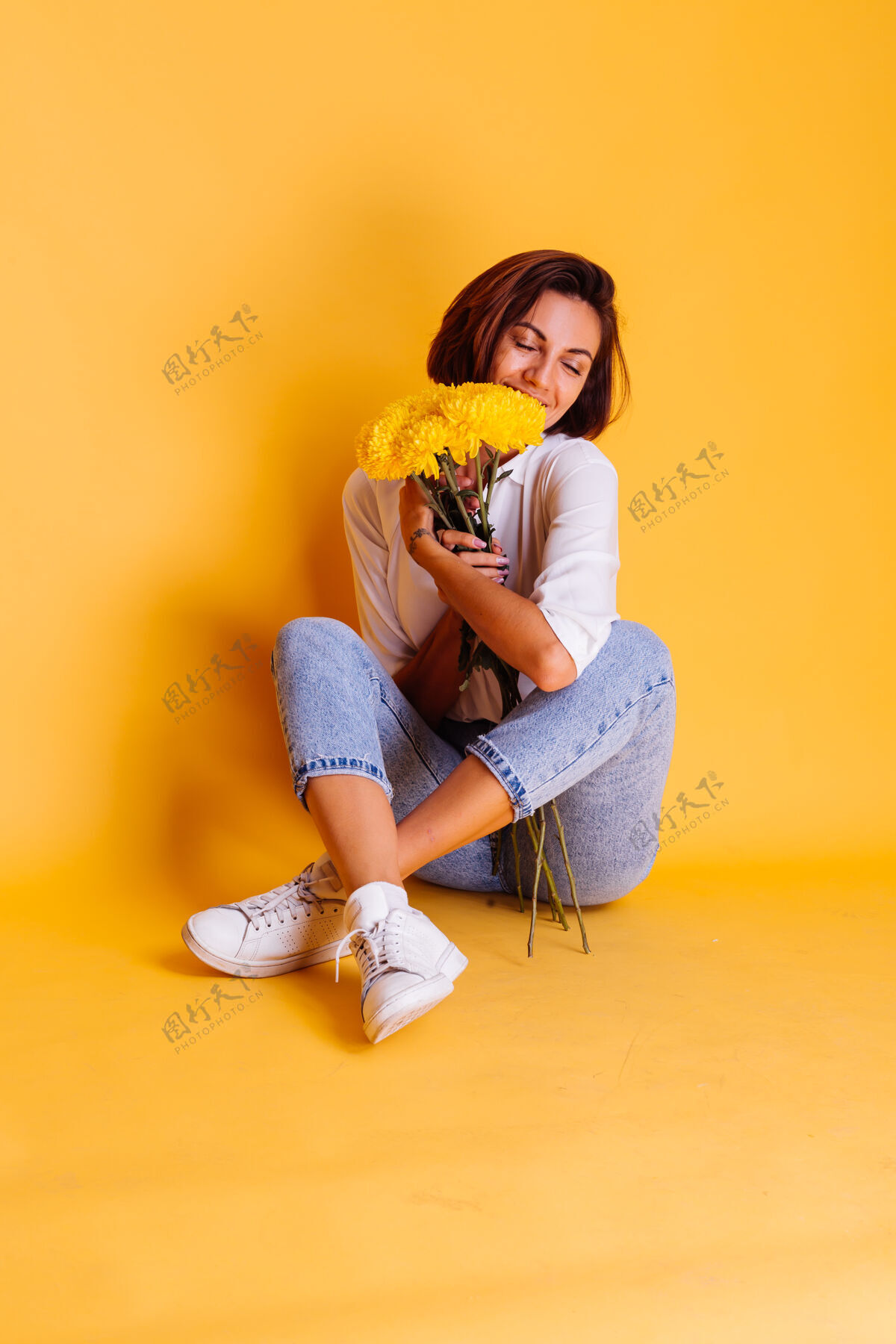 期待摄影棚拍摄的黄色背景快乐的白人妇女短发穿着休闲服白衬衫和牛仔裤手持一束黄色紫苑快乐惊喜微笑