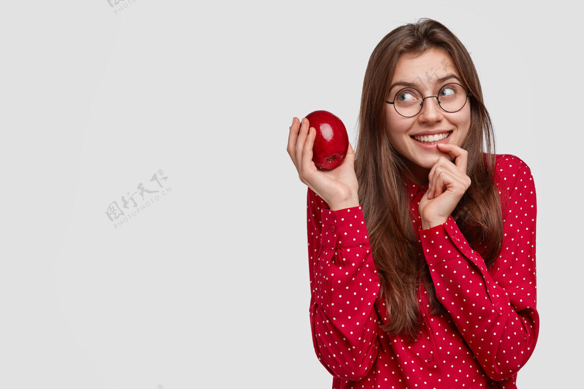 黑发梦幻般的欧洲年轻女士手指贴着嘴唇 捧着新鲜可口的苹果 想着做馅饼舌头果汁素食