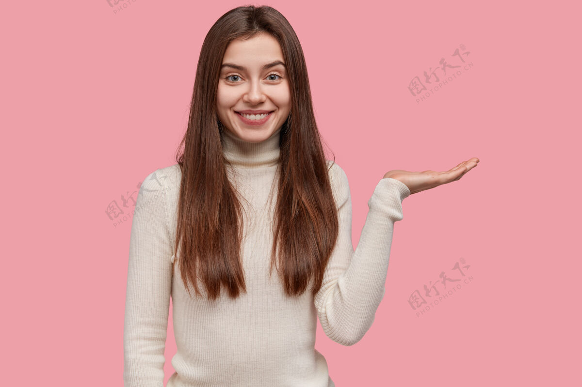 成功快乐女卖家的照片在粉色的空白处举手 穿着休闲服 微笑着 为新产品做广告人手掌广告